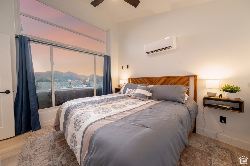 Bedroom with a wall mounted AC, light wood-style floors, and a ceiling fan