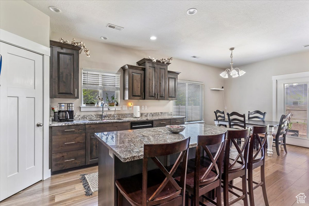 Kitchen with a kitchen bar, light wood-type flooring, dark brown cabinetry, a center island, and recessed lighting