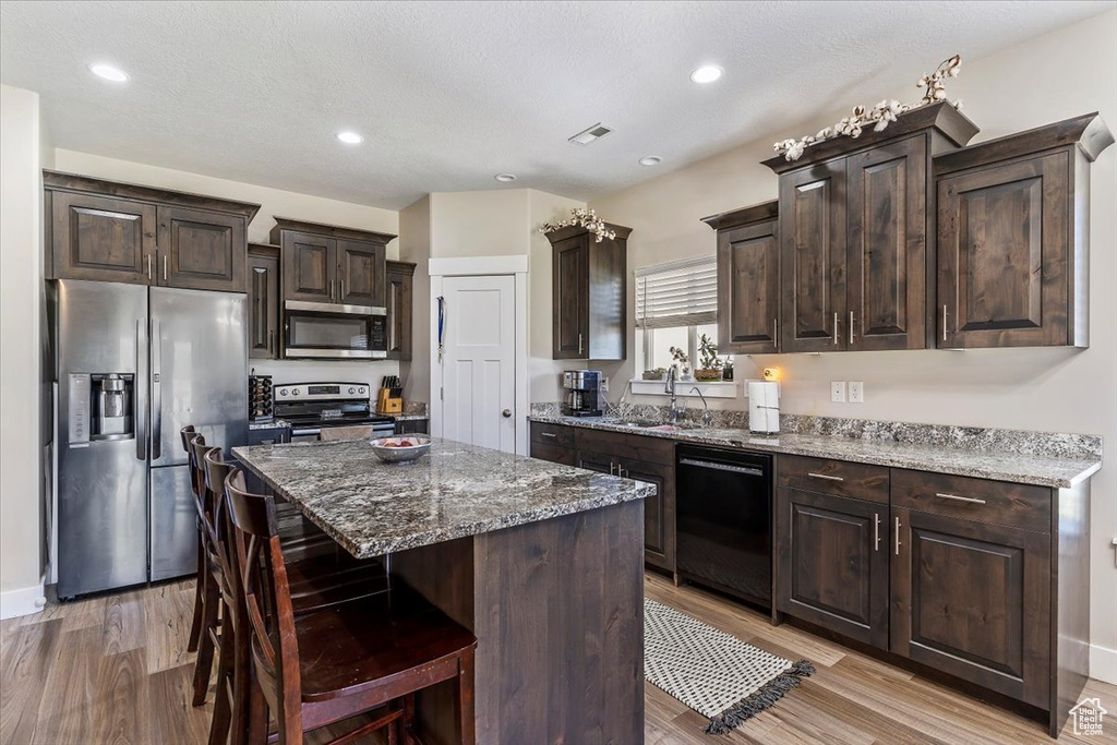 Kitchen featuring stainless steel appliances, light wood-type flooring, dark brown cabinets, a center island, and recessed lighting