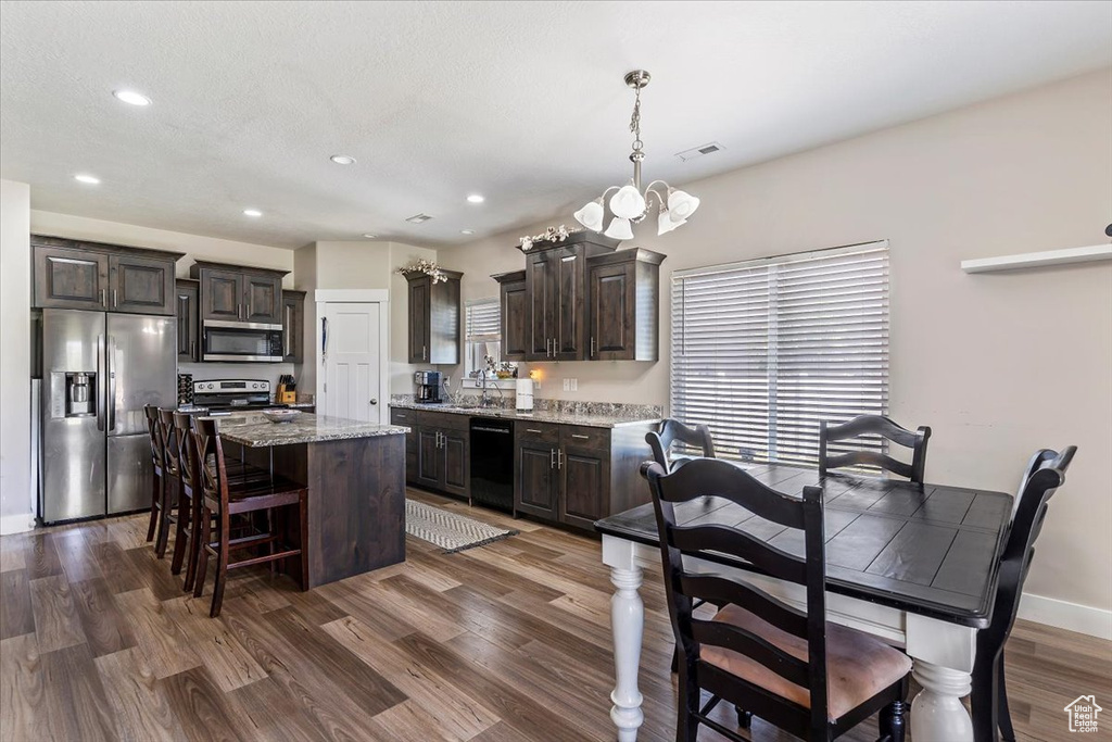 Kitchen with appliances with stainless steel finishes, dark brown cabinetry, a center island, dark wood-style floors, and recessed lighting
