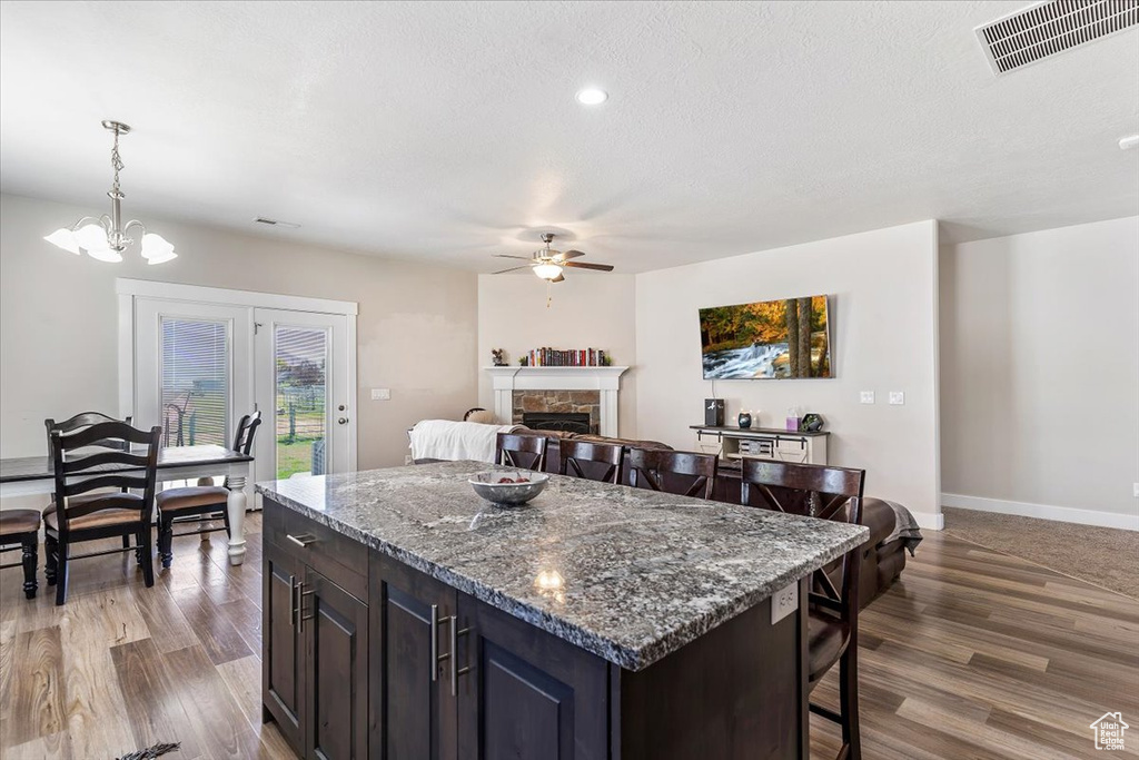 Kitchen featuring a stone fireplace, a ceiling fan, dark wood-type flooring, a breakfast bar, and a kitchen island
