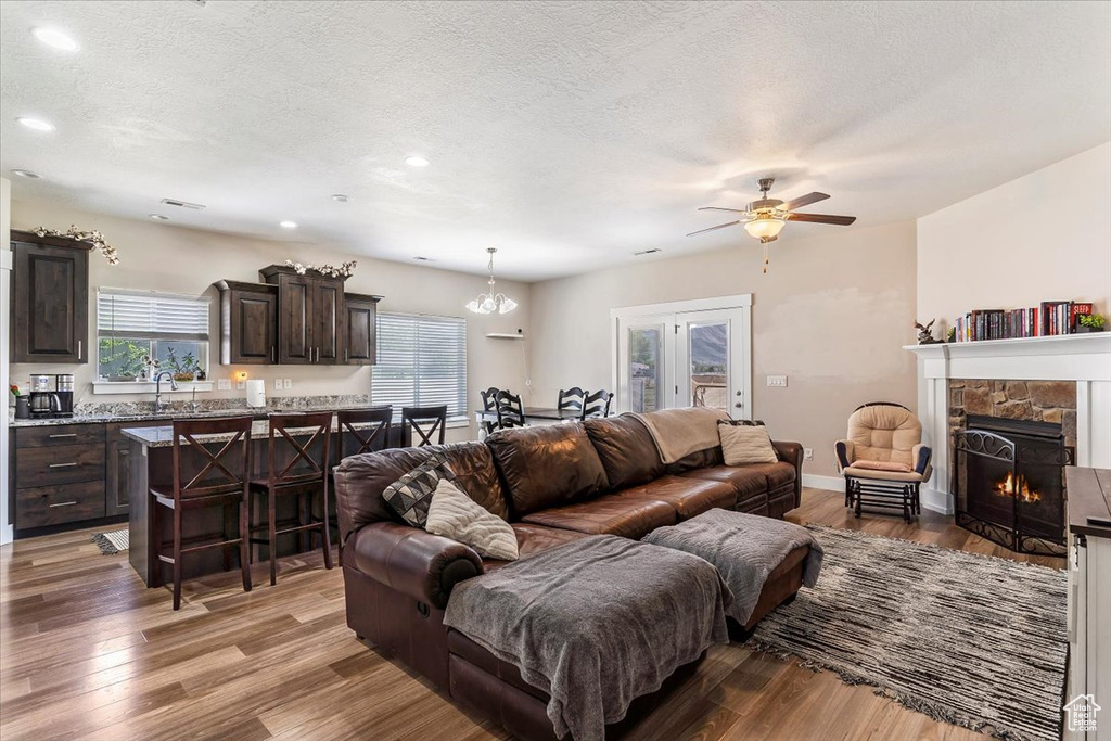 Living area featuring light wood-style floors, recessed lighting, a ceiling fan, a stone fireplace, and a textured ceiling