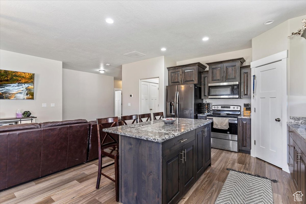 Kitchen with appliances with stainless steel finishes, a breakfast bar, open floor plan, wood finished floors, and a kitchen island