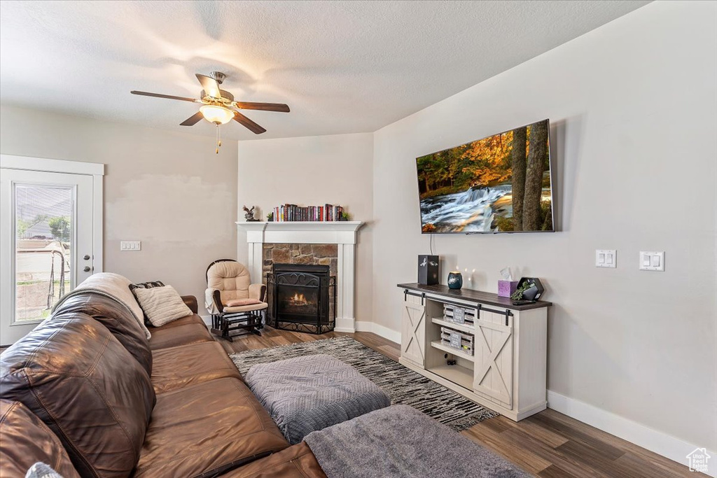 Living room featuring wood finished floors, ceiling fan, and a stone fireplace