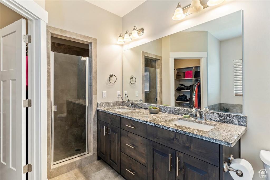 Full bathroom featuring double vanity, a shower stall, a walk in closet, and tile patterned floors