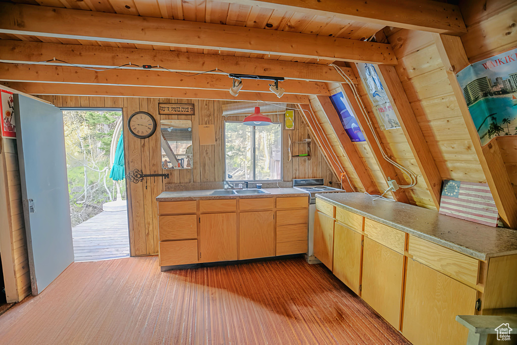 Kitchen with wooden walls, light wood-style floors, lofted ceiling, range, and light brown cabinets