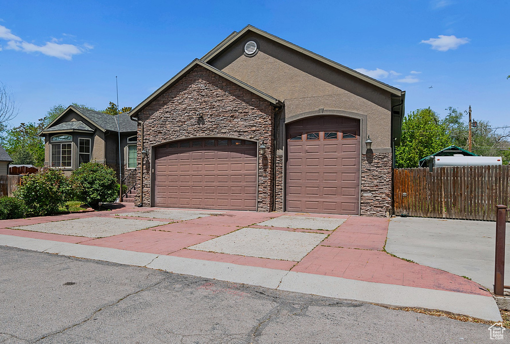 View of front of house with stone siding, a garage, driveway, and stucco siding