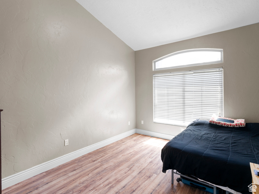 Bedroom with light wood finished floors and lofted ceiling
