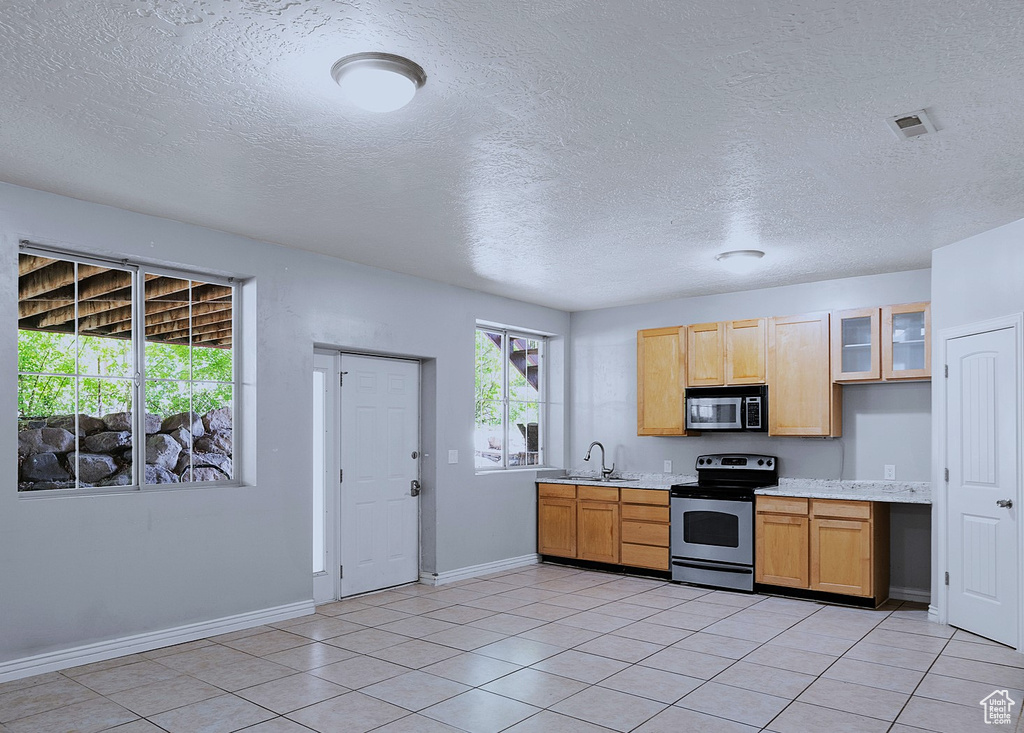 Kitchen with stainless steel appliances, light countertops, a textured ceiling, light tile patterned flooring, and glass insert cabinets