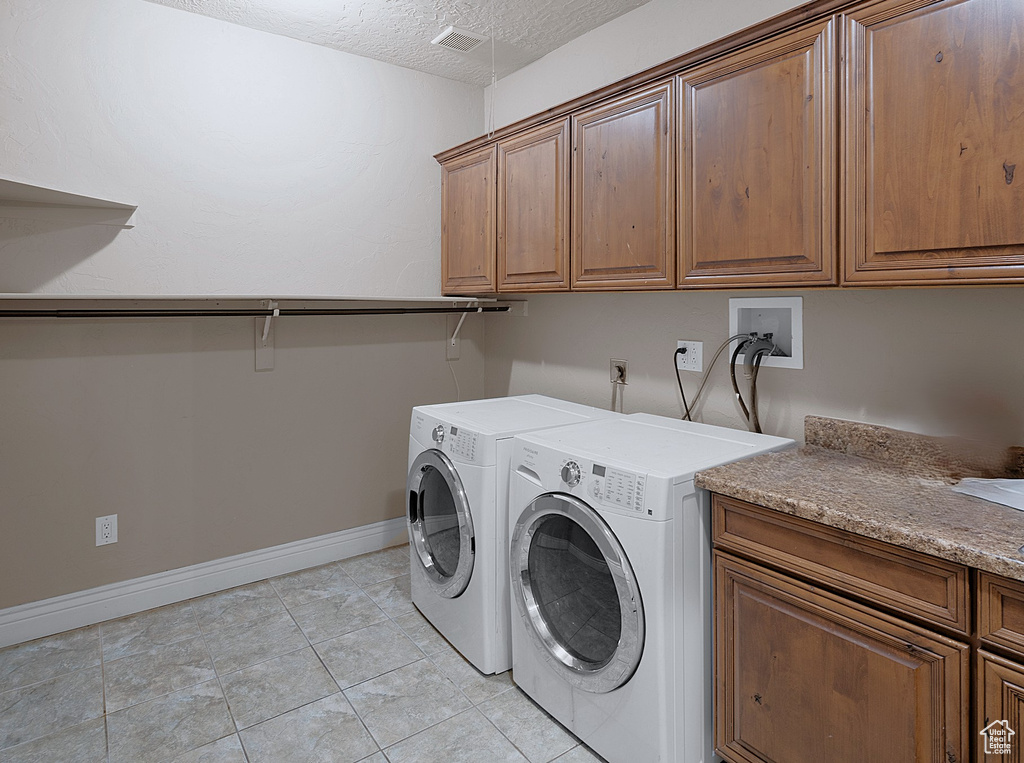 Laundry room with cabinet space, washer and clothes dryer, a textured ceiling, and light tile patterned floors