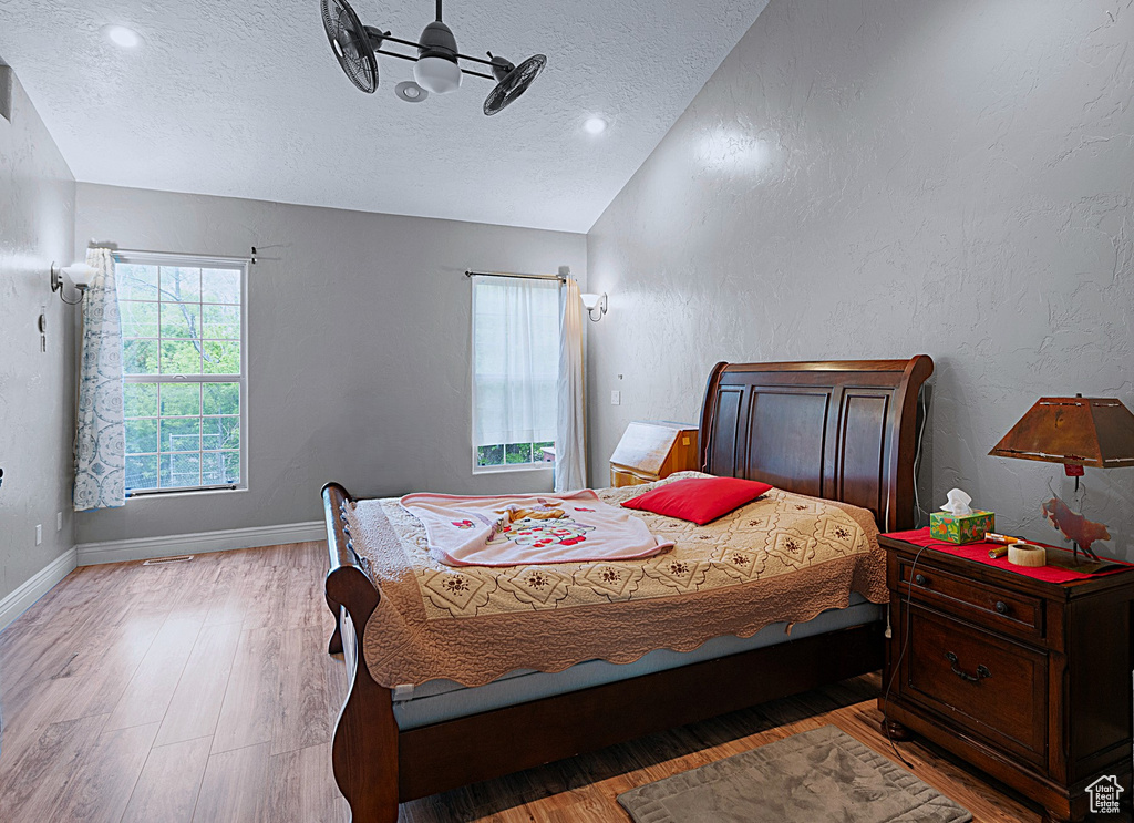 Bedroom featuring lofted ceiling, a textured ceiling, wood finished floors, and a textured wall