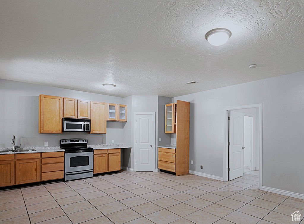 Kitchen featuring stainless steel appliances, light countertops, glass insert cabinets, light tile patterned flooring, and a textured ceiling