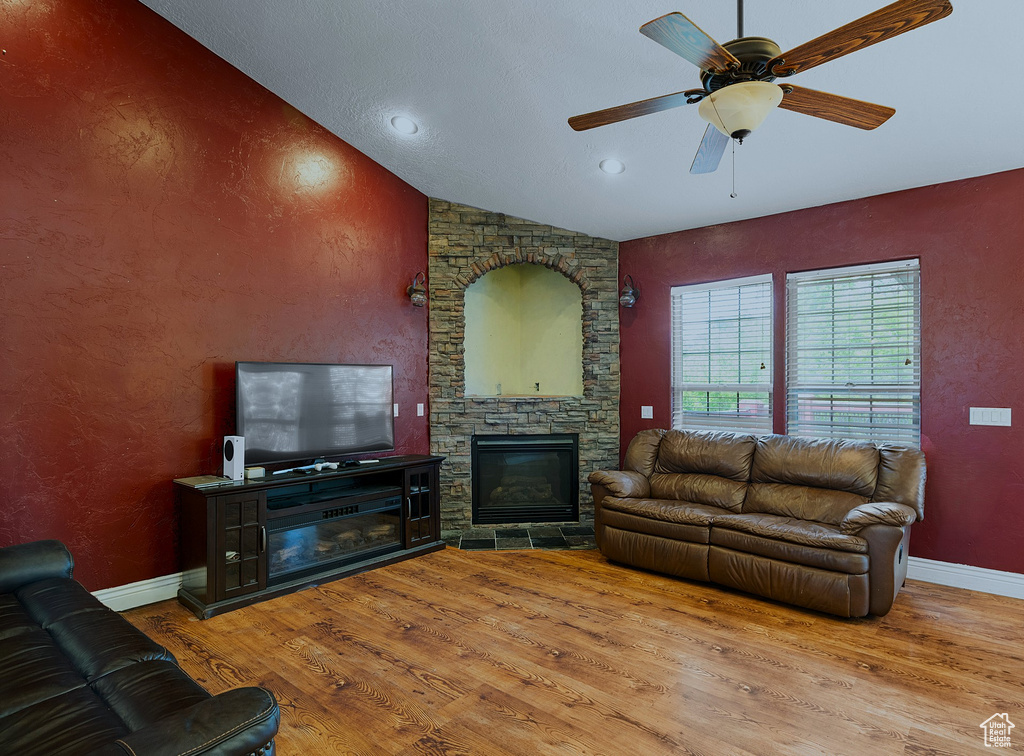 Living room with wood finished floors, a ceiling fan, a stone fireplace, vaulted ceiling, and recessed lighting
