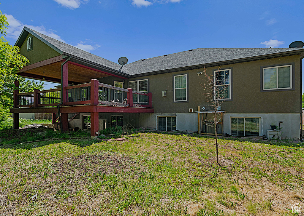 Rear view of house featuring a wooden deck, a yard, and stucco siding