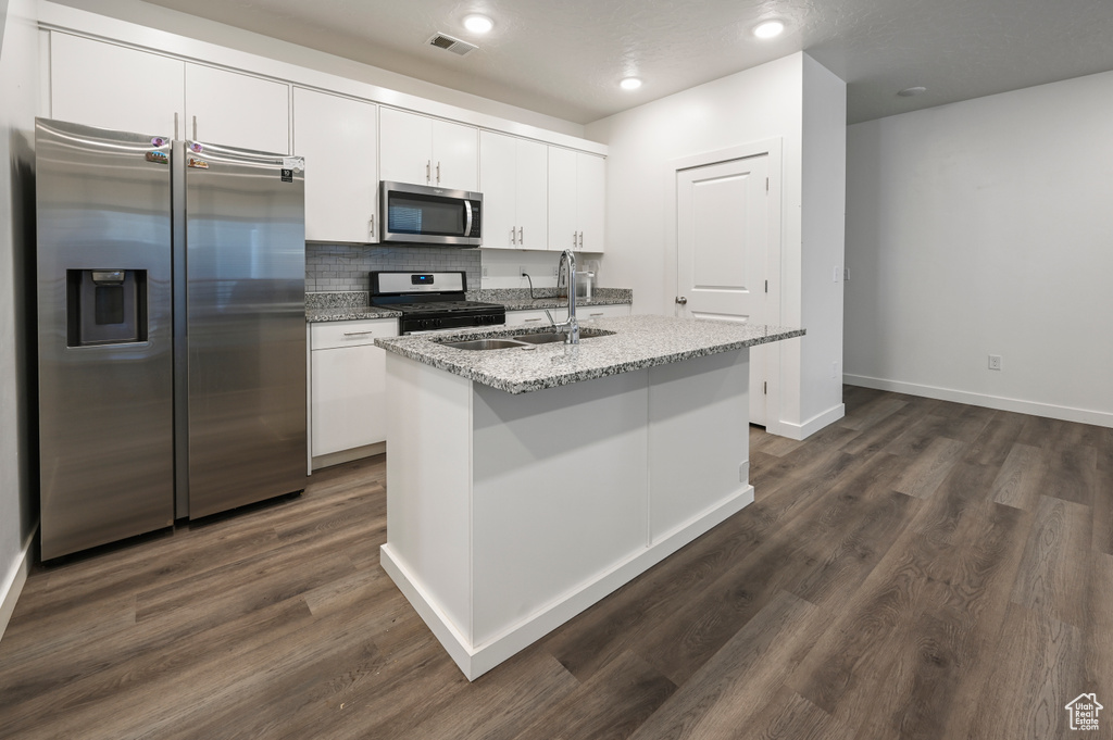 Kitchen with appliances with stainless steel finishes, white cabinetry, a kitchen island with sink, light stone counters, and tasteful backsplash