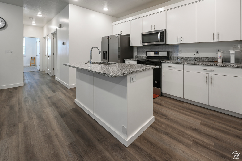 Kitchen featuring appliances with stainless steel finishes, an island with sink, dark wood finished floors, white cabinets, and decorative backsplash