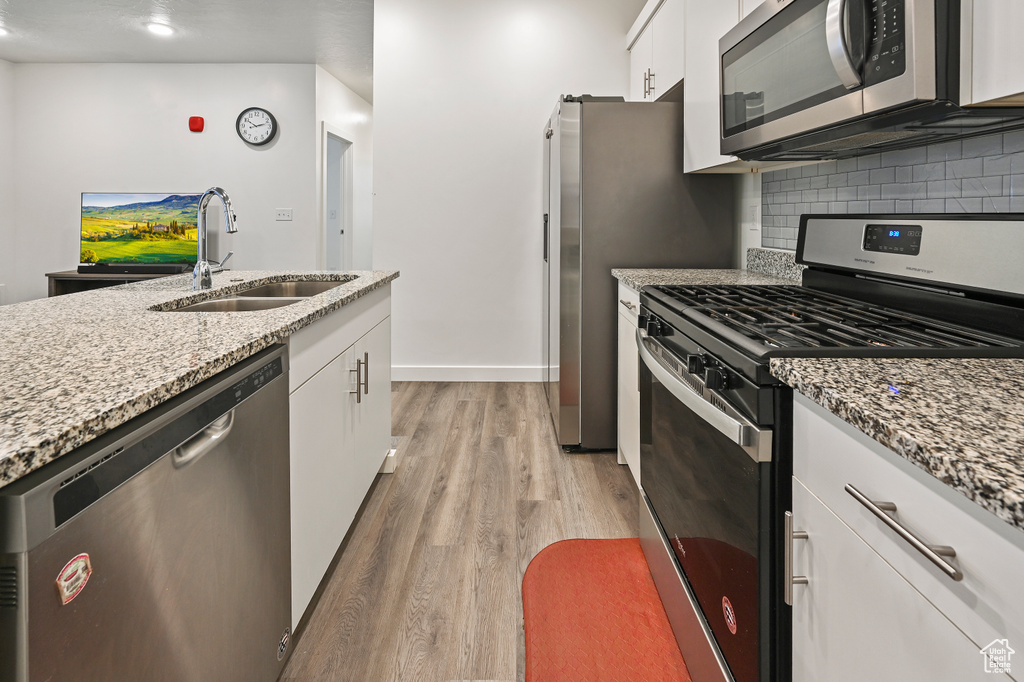 Kitchen with stainless steel appliances, light wood finished floors, decorative backsplash, white cabinetry, and light stone counters