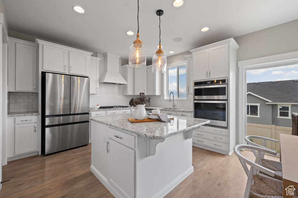 Kitchen featuring appliances with stainless steel finishes, custom range hood, white cabinetry, a center island, and a wainscoted wall