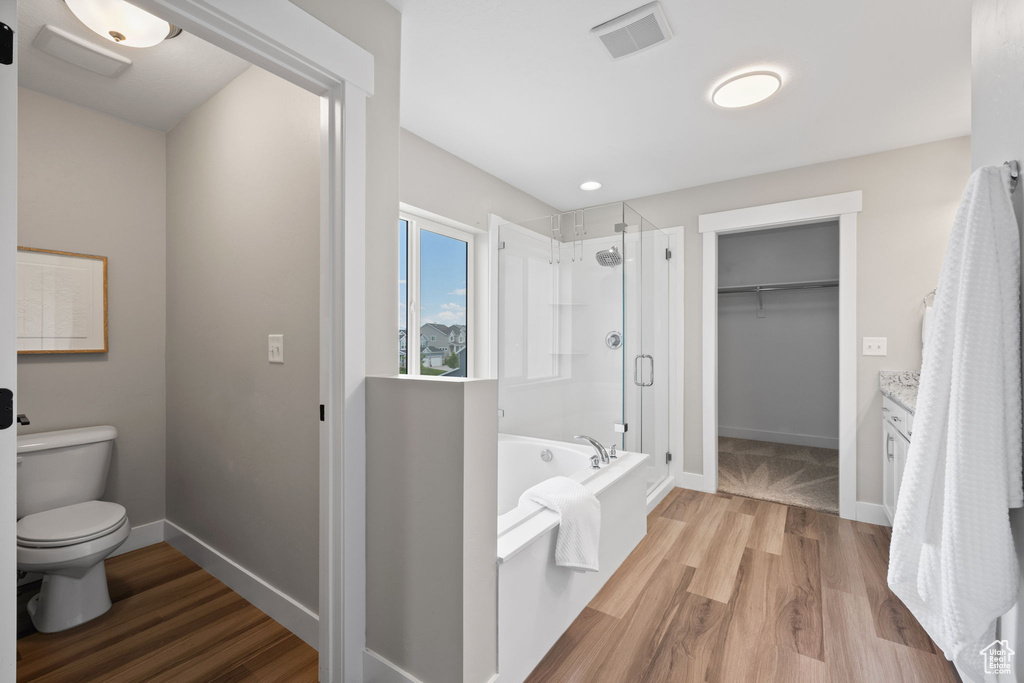 Full bath with a shower stall, a walk in closet, a bath, and wood finished floors