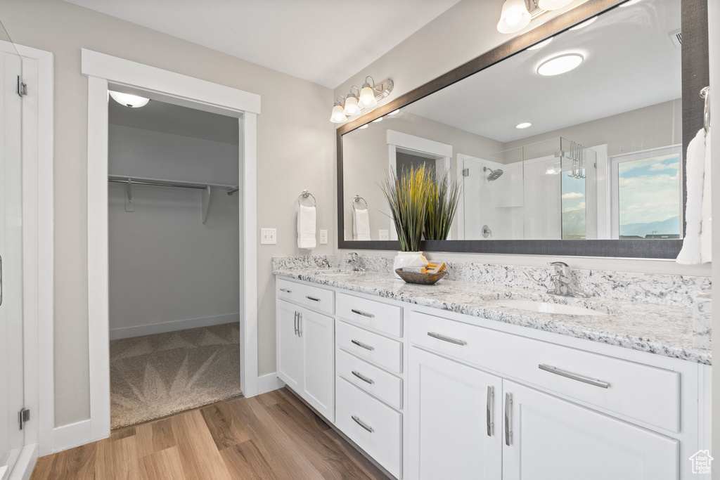 Full bath with a stall shower, double vanity, a spacious closet, and wood finished floors