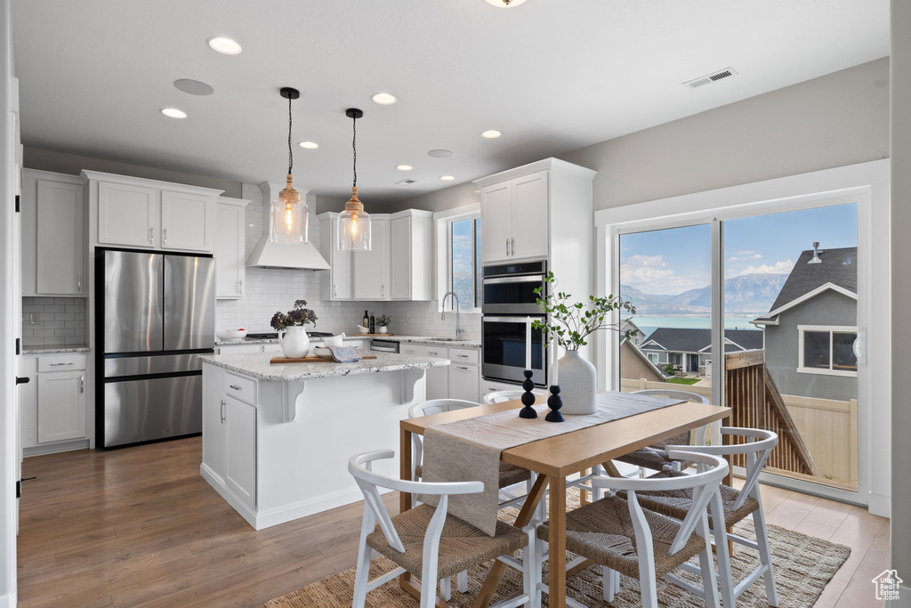 Kitchen with stainless steel appliances, wall chimney exhaust hood, a kitchen island, backsplash, and recessed lighting