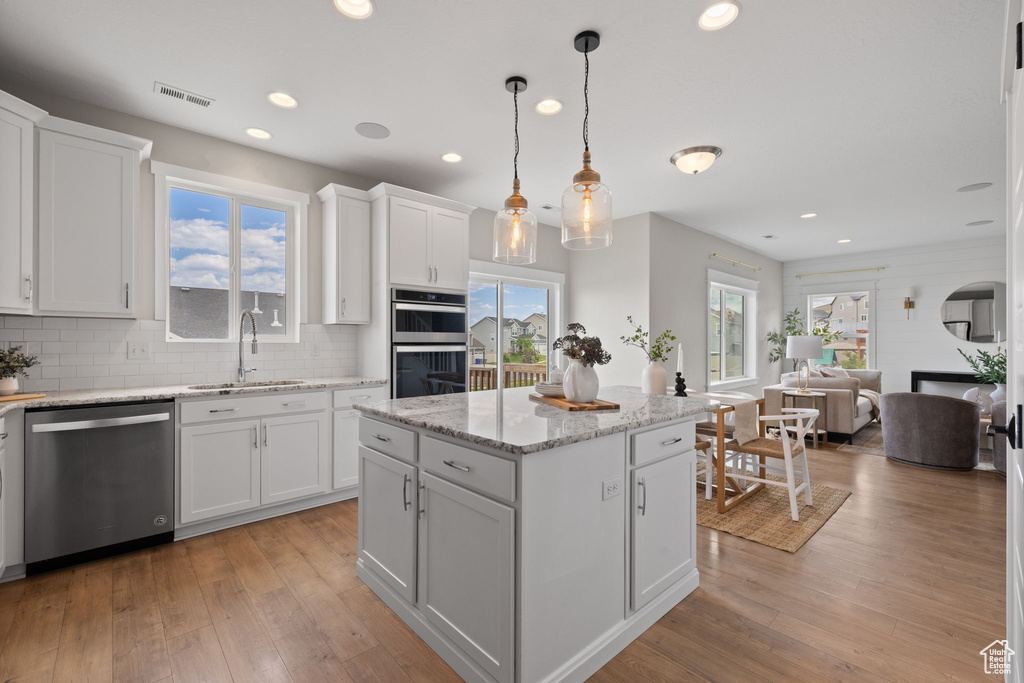 Kitchen with stainless steel appliances, light wood finished floors, decorative backsplash, white cabinetry, and recessed lighting