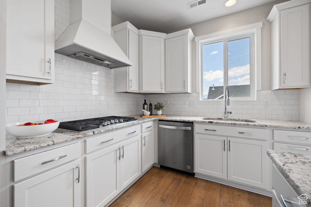 Kitchen with appliances with stainless steel finishes, custom exhaust hood, white cabinets, and backsplash