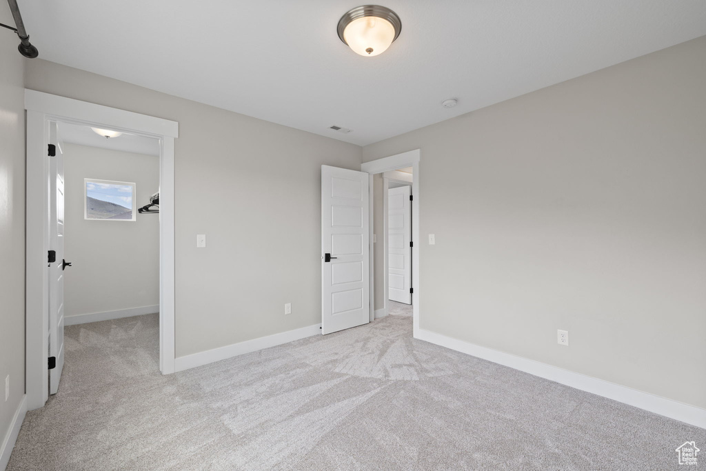 Unfurnished bedroom with light colored carpet and a walk in closet