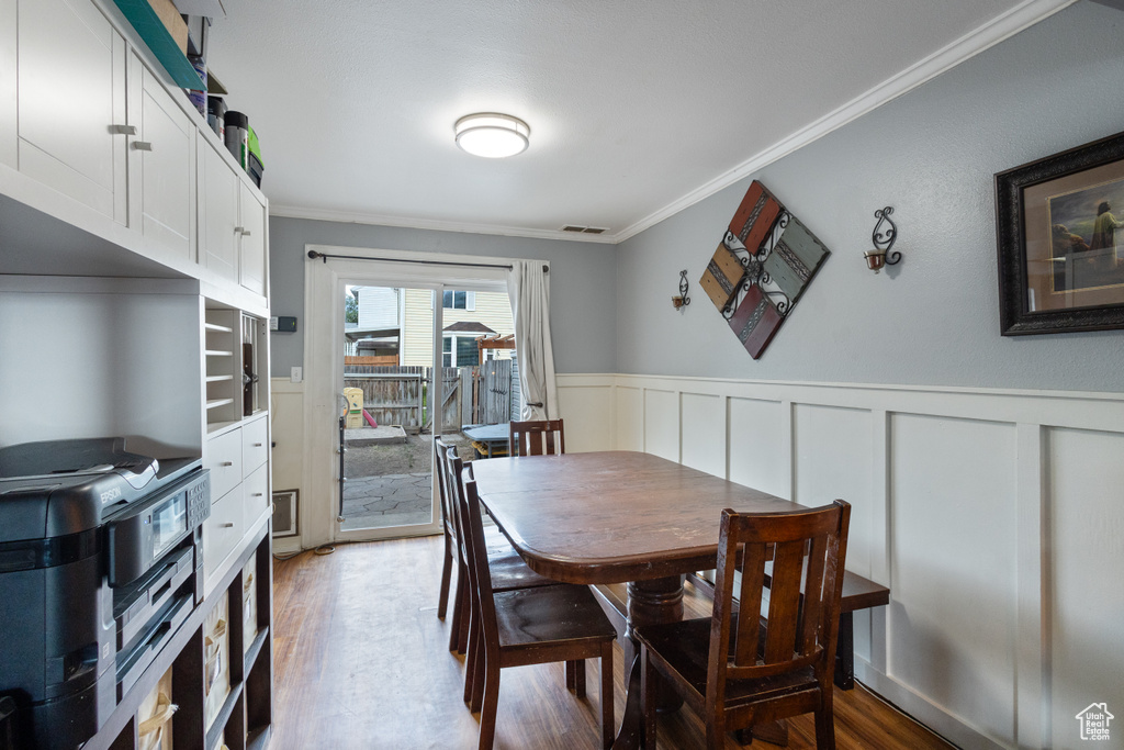 Dining area with crown molding, light wood-type flooring, wainscoting, and a decorative wall