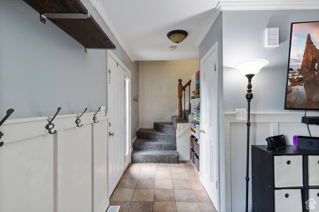 Stairway with crown molding, wainscoting, carpet flooring, and a decorative wall
