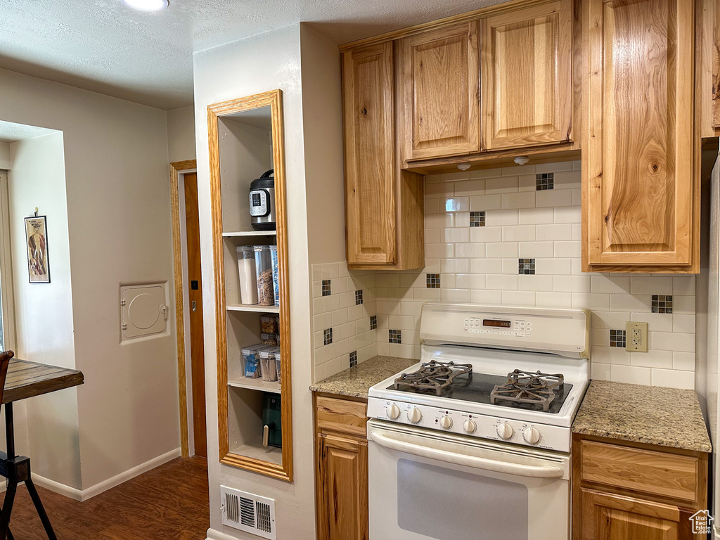 Kitchen with white gas range, decorative backsplash, wood finished floors, light stone countertops, and a textured ceiling