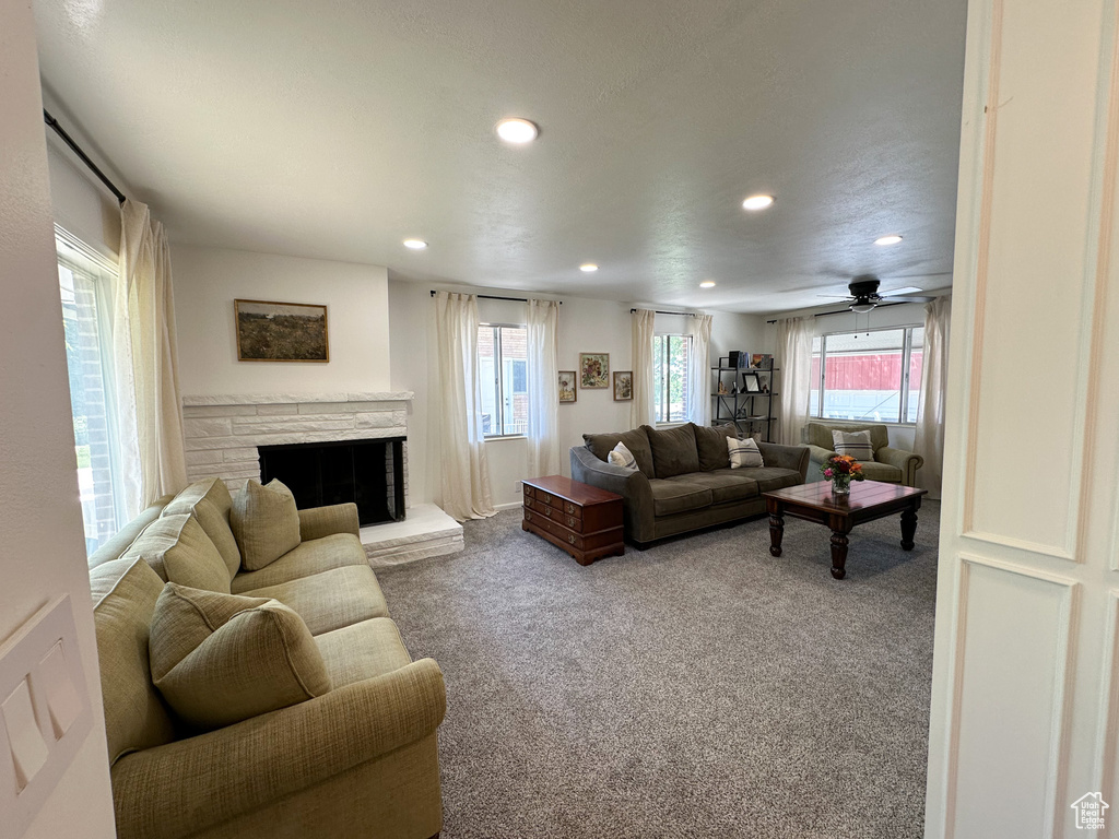 Carpeted living room featuring recessed lighting, healthy amount of natural light, a stone fireplace, and a ceiling fan
