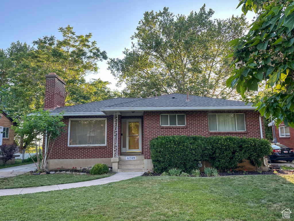 Ranch-style home with brick siding, a front yard, a chimney, and a shingled roof