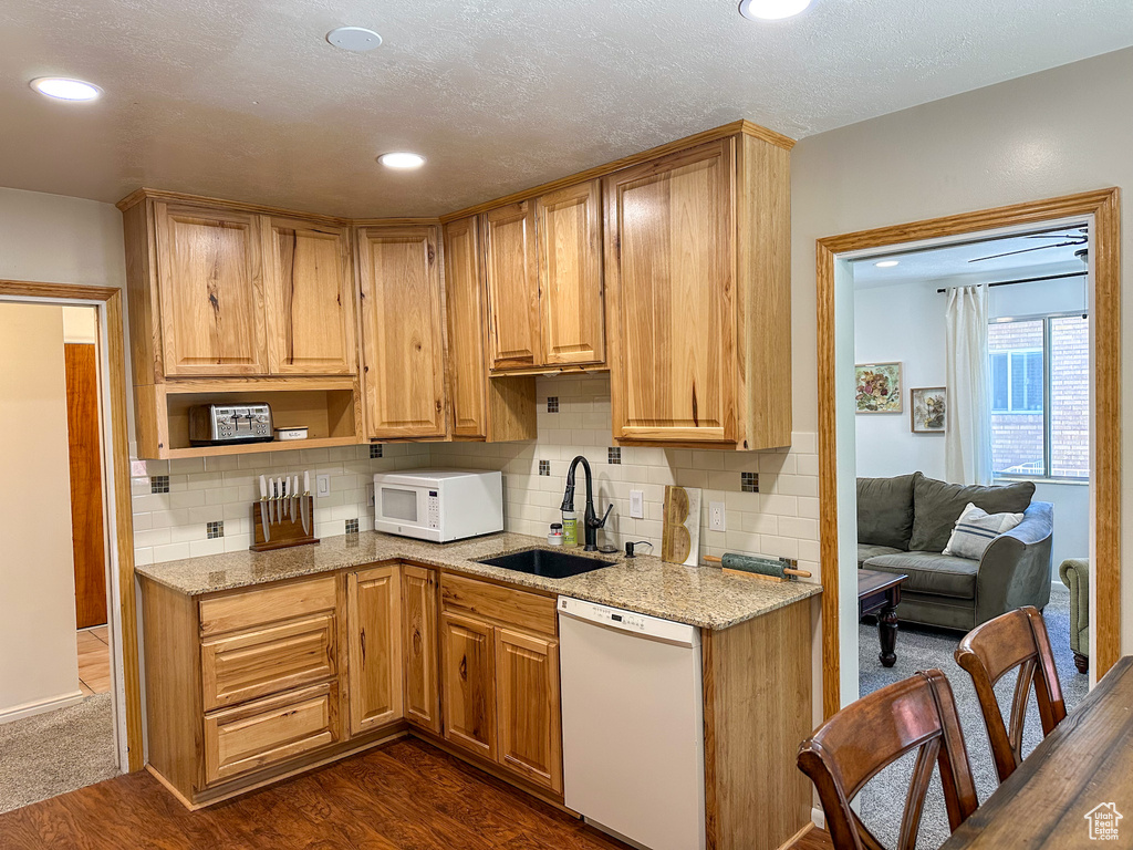 Kitchen with white appliances, decorative backsplash, light stone countertops, dark wood-type flooring, and recessed lighting