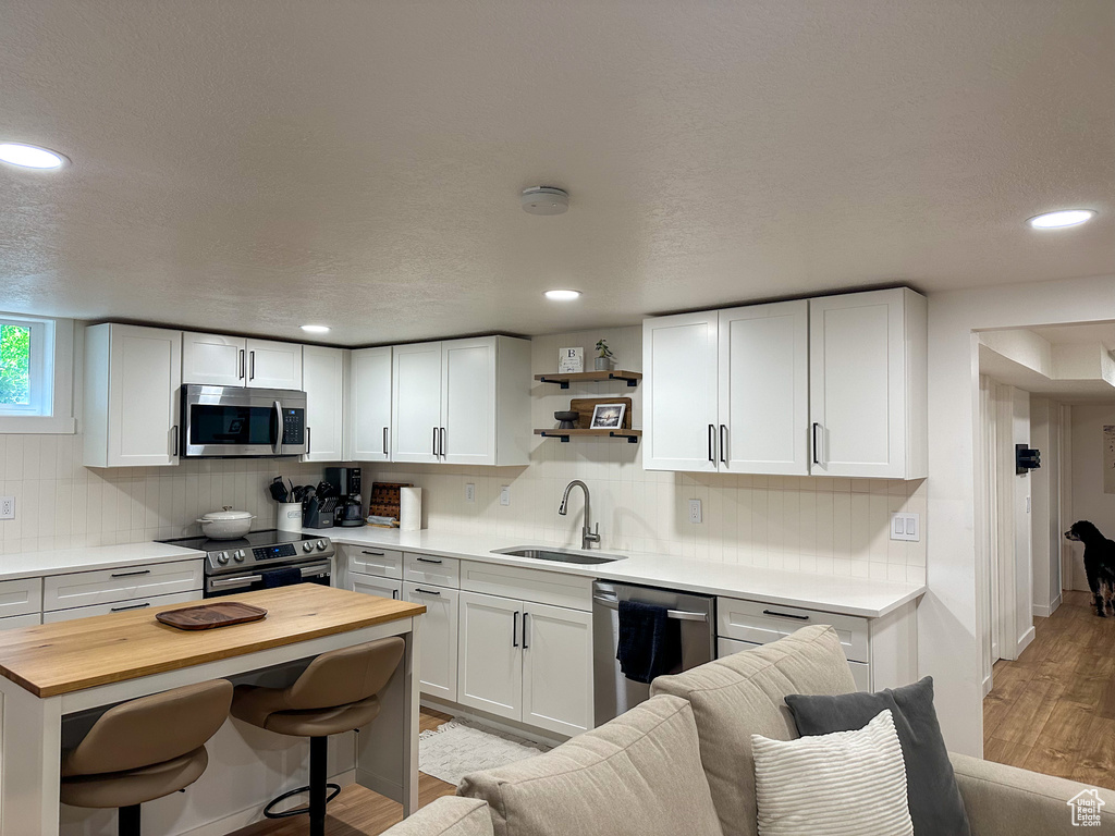 Kitchen featuring stainless steel appliances, butcher block counters, light wood-style flooring, a kitchen bar, and white cabinets