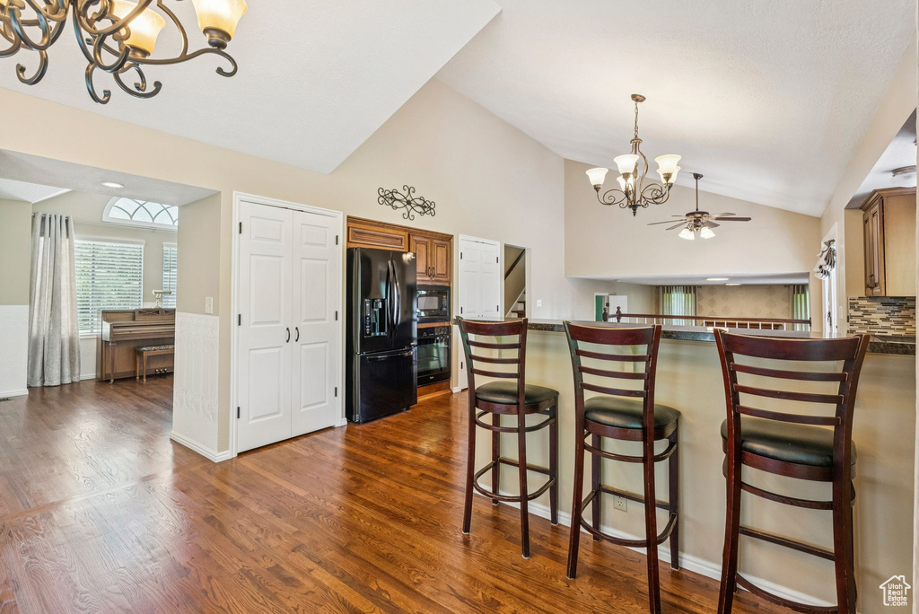 Kitchen featuring black appliances, a chandelier, vaulted ceiling, dark wood finished floors, and dark countertops