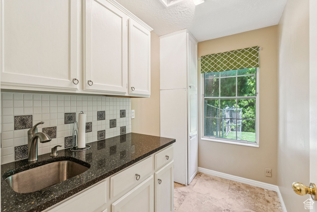 Kitchen with decorative backsplash, white cabinetry, dark stone counters, and a textured ceiling