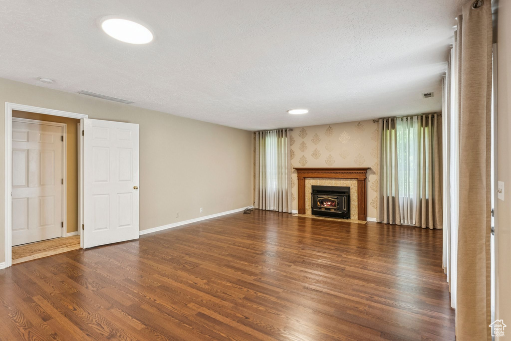 Unfurnished living room featuring wood finished floors, a fireplace with flush hearth, and a textured ceiling