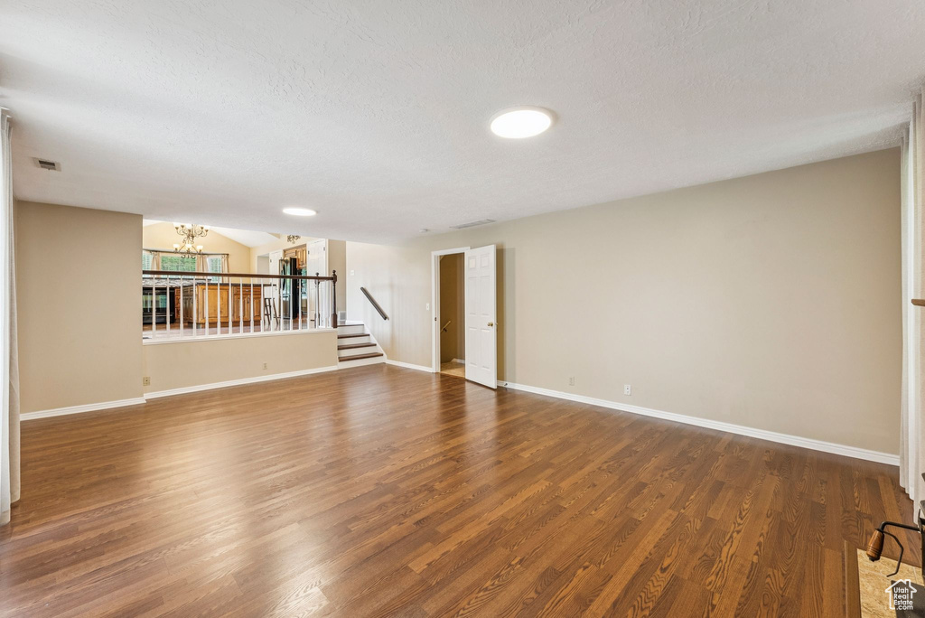 Empty room featuring a chandelier, wood finished floors, stairs, and a textured ceiling