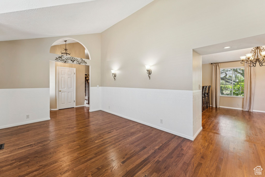 Unfurnished room with a chandelier, wood finished floors, and high vaulted ceiling