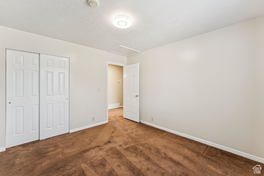 Unfurnished bedroom featuring carpet, a closet, attic access, and a textured ceiling
