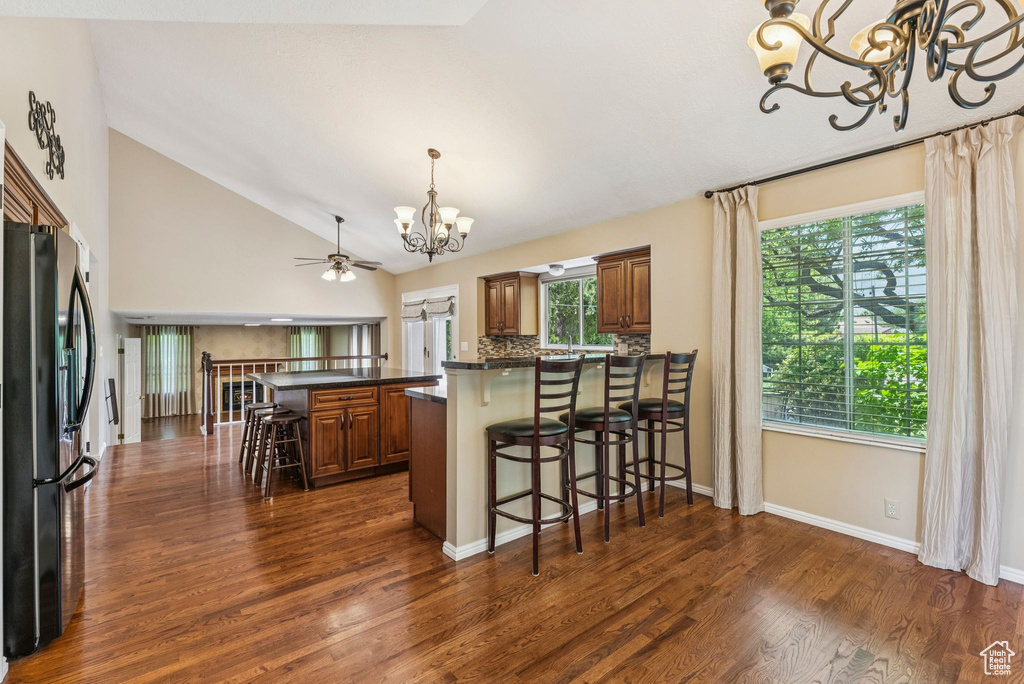 Kitchen with a chandelier, refrigerator with ice dispenser, brown cabinetry, dark countertops, and lofted ceiling