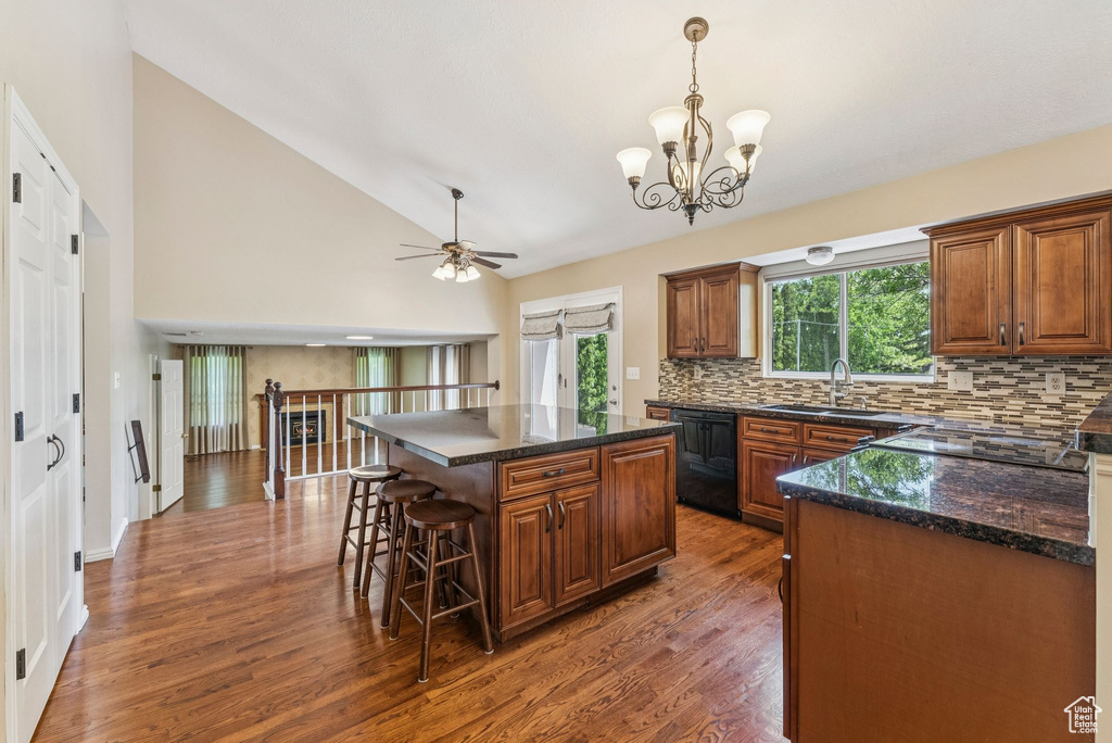 Kitchen with black dishwasher, backsplash, dark wood-style flooring, a chandelier, and a kitchen breakfast bar