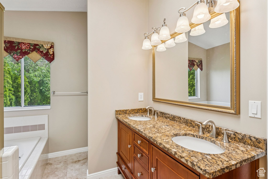 Full bath with double vanity, a chandelier, and a relaxing tiled tub