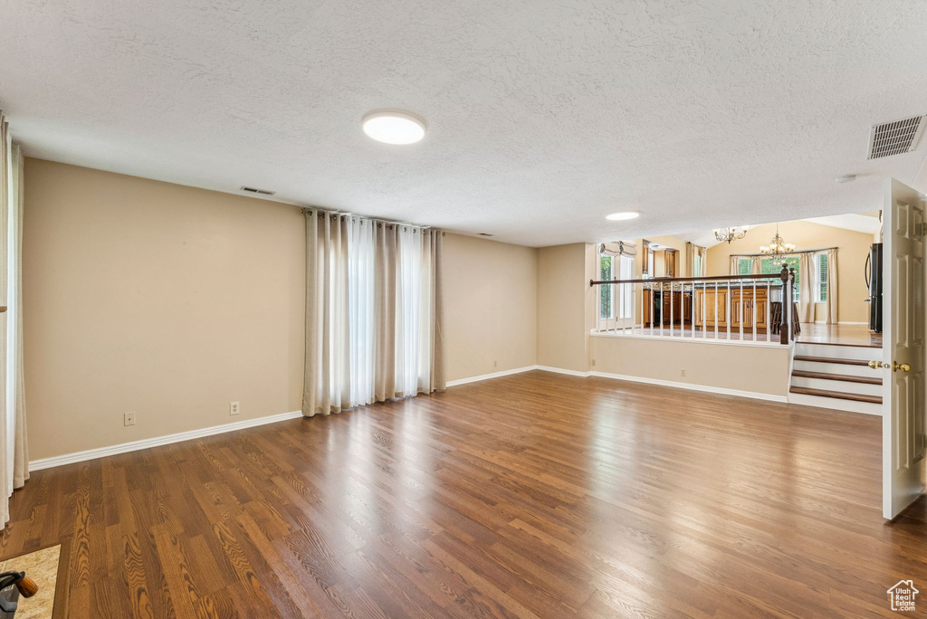Unfurnished living room with a chandelier, a textured ceiling, and wood finished floors