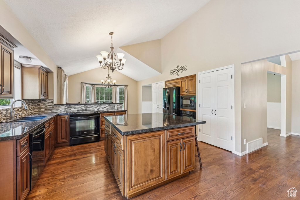 Kitchen with black appliances, a chandelier, vaulted ceiling, decorative backsplash, and brown cabinets