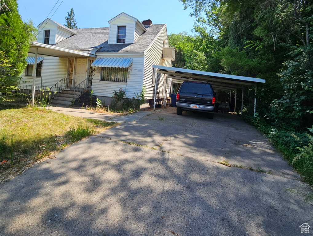 Cape cod house with a detached carport, concrete driveway, roof with shingles, and a chimney