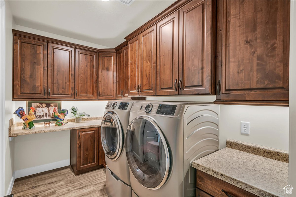 Laundry room with washing machine and clothes dryer, cabinet space, and light wood finished floors
