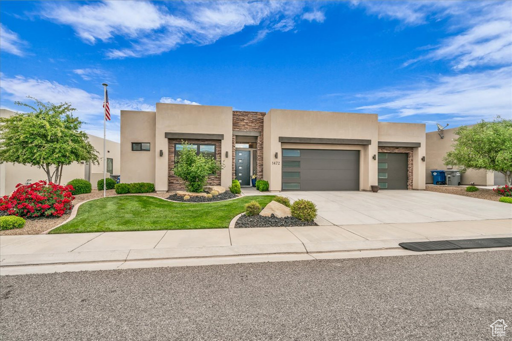 Pueblo revival-style home featuring stucco siding, a garage, stone siding, concrete driveway, and a front lawn