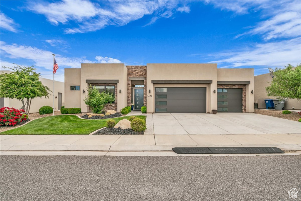Southwest-style home featuring stucco siding, an attached garage, driveway, stone siding, and a front yard
